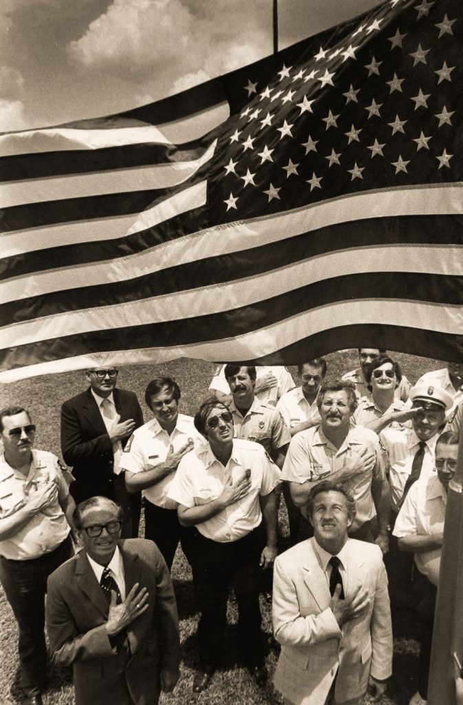 1983-85: Fire Chief Herman Rice, Mayor Ron Blatchley and others salute a flag given to the city by E.C. Oates of the Elks Lodge.